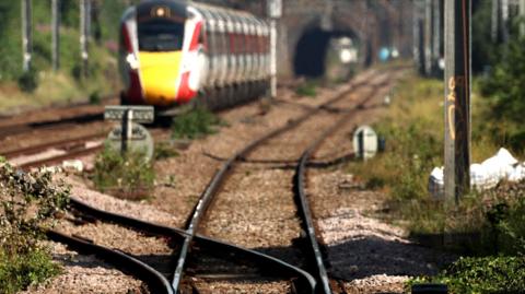 Train tracks up close with a tunnel and train in the background, blurred.