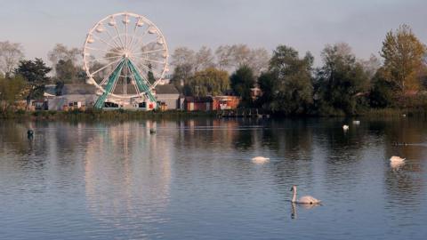 Lake and Ferris Wheel at Billing Aquadrome on a clear and calm autumn day. Waterfowl including swans are swimming on the lake.