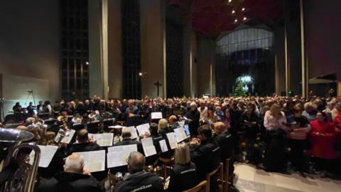 A brass band playing inside a cathedral in front of a large audience