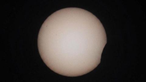 The start of the solar eclipse in Braunton, Devon. The shadow of the moon can be seen starting to cover the edge of the sun in the bottom right. The Sun is seen as a white circle on a black background.