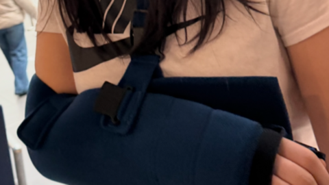 A close up shot of a girl's arm in a navy blue sling. Her white Nike T-shirt is visible, and her dark brown hair.