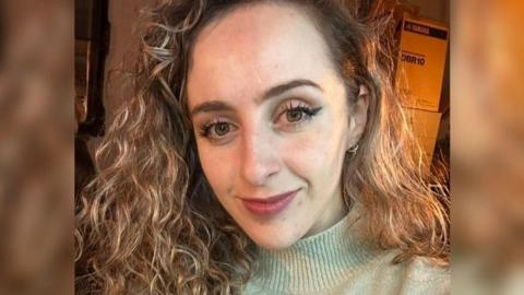 Marianne Ward wearing a light green jumper, she has curly hair and is smiling.