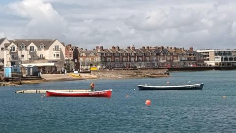 Grey clouds over a seaside town with a red and a blue boat on the water 