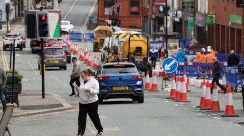 The high street in Ashton-in-Makerfield with pedestrians and roadworks.