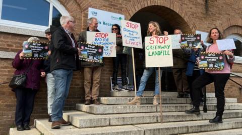 People standing on the steps of County Hall in Exeter with signs protesting against the proposed landfill site 