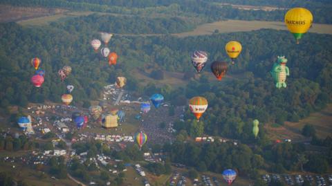 A large array of hot air balloons of all shapes and colours flying from Ashton Court Estate during sunset.