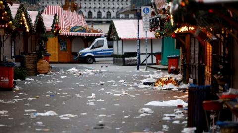 A pedestrian walkway through a Christmas market is littered with rubbish and other debris