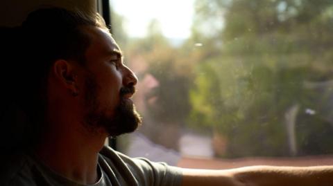 Side view of a man traveling on a train alone, looking through the window pensive, enjoying the view. - stock photo