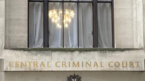 The front of the Old Bailey with the words Central Criminal Court in gold and  illuminated lamps showing though the window.