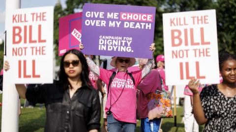 Campaigners on both sides of the assisted dying debate hold up placards outside Parliament in June 2025. One reads: "Kill the bill not the ill", while another reads: "Give me choice over my death".
