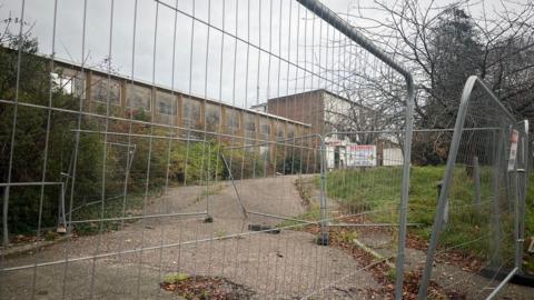 Metal fencing in front of the boarded up and derelict old police station site on Heavitree Road in Exeter.