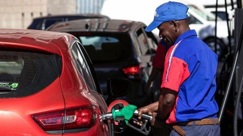 A petrol attendant in red and blue uniform fills a red car