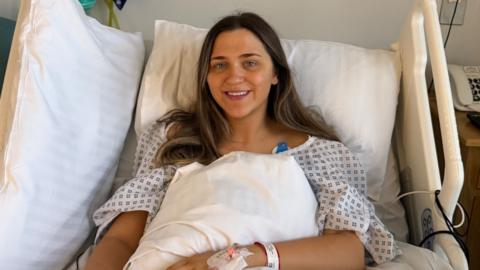 A women in a hospital bed wearing a blue and white gown.