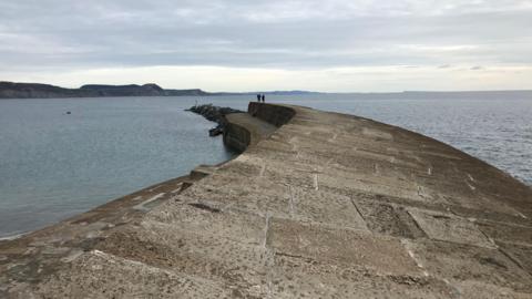 The top of the cobb as it runs into the sea. There are people at the end of it going for a walk.