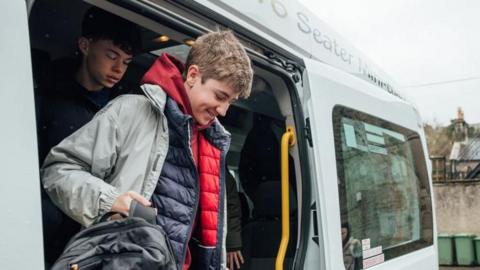 Two teenage boys get out of a minibus