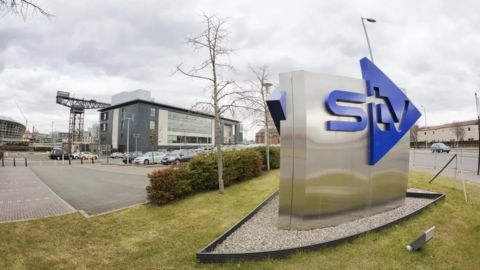 An STV sign outside the HQ building in Glasgow with the Finnieston Crane and the Hydro in the background