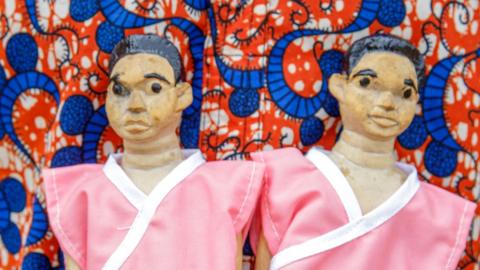 A man holds a pair of figurines dressed in matching clothes. 