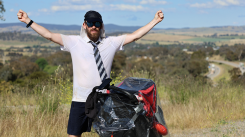 Rob Pope is standing with his arms aloft, beside the pram.