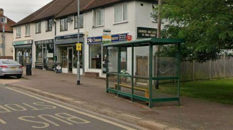 the bus stop and shelter on a  road with some shops behind