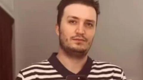 A man with dark hair wearing a black and white T-shirt.
