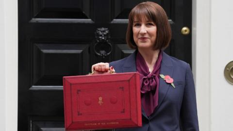 Rachel Reeves, wearing a dark suit, holds up a red box outside 10 Downing Street 