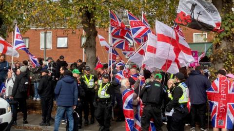 A gathering of protesters, many holding union flags and St George's flags with police mingling
