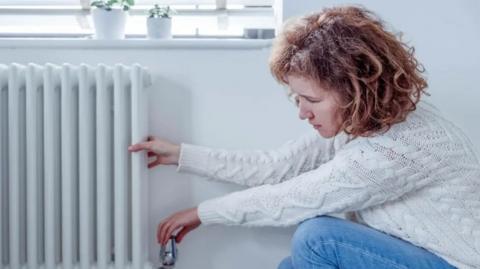 A woman turning the dial on a radiator in a home.