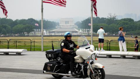 A US Park Police officer sits on a motorbike in front of the Washington Monument, with American flags in the background