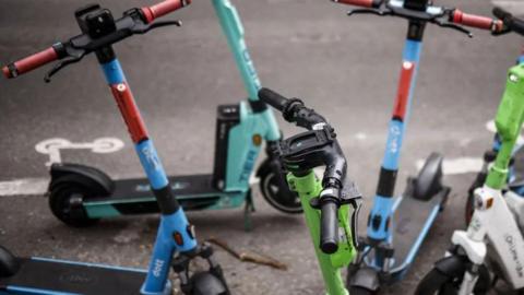 Six brightly coloured e-bikes parked on a pavement