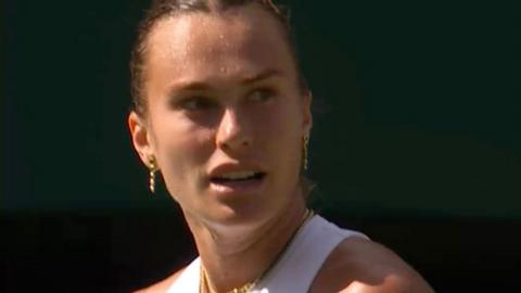 Aryna Sabalenka looks to the right - she has brown hair pulled back and wears a white vest top