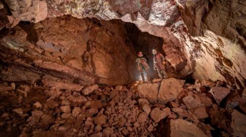 two cavers in helmets standing in a big orange cave