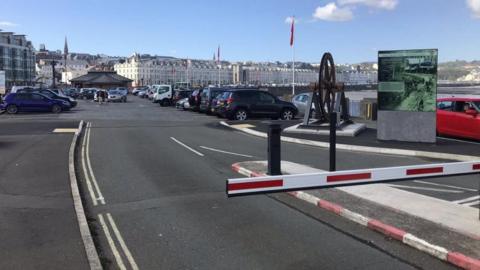 A view of the Bottleneck car park at the end of Loch Promenade. There is a red and white barrier to the right and cars parked in rows.
