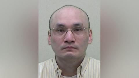 Mugshot of Kwan. he is bald and wearing glasses