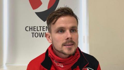 Liam Kinsella sitting in front of a Cheltenham Town badge
