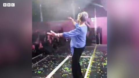 Anne dances on stage in a purple jumper and black trousers