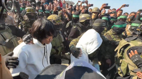 Two Thais taken hostage by Hamas are freed in Khan Yunis on January 30, 2025 - grab from video by BBC Gaza freelancer. Two men wearing white hoodies are surrounded by masked guards and people trying to take their pictures with their mobile phones