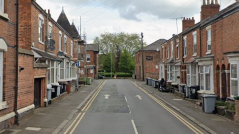 Streetview shot of a street of traditional terraced properties, many with bins outside.