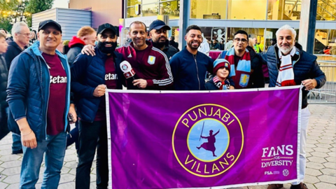 A group of men and one child stand behind a large banner, smiling. The banner reads Punjabi Villans, fans for diversity