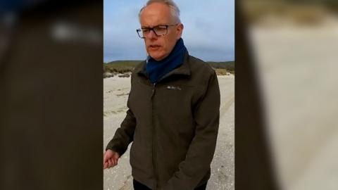 Man walks along sandy beach wearing a green jacket