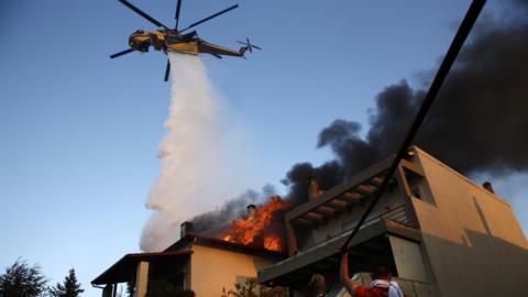 A firefighting helicopter and volunteers battle to put out a fire burning houses in the residential area of Kryoneri, in the suburbs of Athens, Greece, 26 July 202