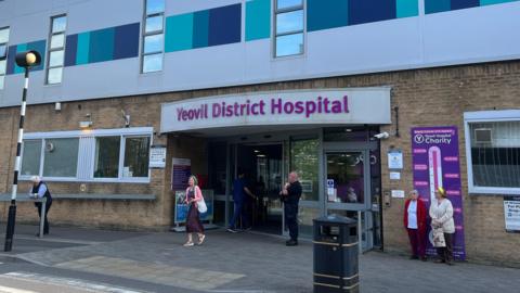 The entrance to Yeovil District Hospital. A few people are standing around the entrance. 