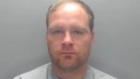 Mugshot of Johnson. He has faint light stubble and a receding hairline with blond hair swept across the top of his head.