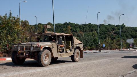 An Israeli military vehicle drives near Sasa in Israel as smoke rises in the background after a missile strike
