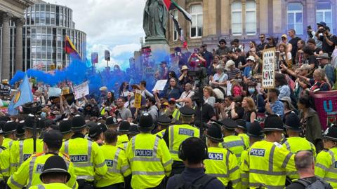 A large amount of police officers in high-vis jackets face a large crowd of people protesting the presence of Britain First in Birmingham's Victoria Square