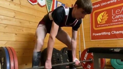 Harvey Chester preparing to lift a barbell with red and blue plates on the ends