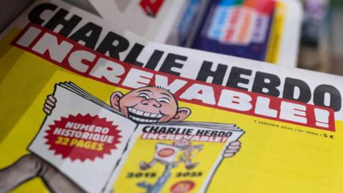 Partial picture of the Charlie Hebdo special edition. Yellow cover, depicting a man reading the magazine (with the same cover of this issue)