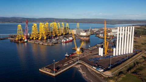 The port has a large number of offshore wind farm structures including long white towers and yellow foundations