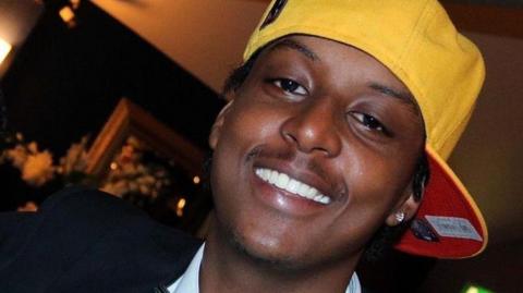 Eddie Kinuthia, pictured smiling at the camera. He is wearing a yellow cap with a red lining turned sideways on his head.