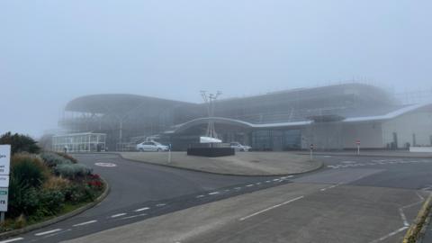 Guernsey Airport seen during thick fog. The photo has been taken from outside the airport on the road about 100m from the main building. It is difficult to see the top of the building. 