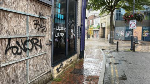 A boarded shop front covered in graffiti on Bridge Street, Swindon